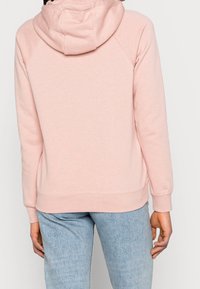 Light pink hoodie with a relaxed fit, featuring a double-layered hood, ribbed cuffs, and hem. Made from soft, textured fabric.