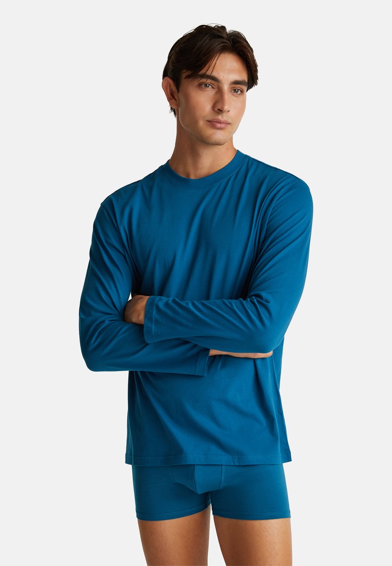 Blauwe lange mouwen shirt met een ronde hals, gecombineerd met bijpassende boxershorts. Zachte stof, aansluitend ontwerp en minimale stikseldetails.