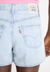 Vaaleansiniset farkkushortsit, joissa on repsottava helma, kaksi takataskua ja Levi's-tunnus vyötäröllä. Sisältää kontrastiväristä ommelta.