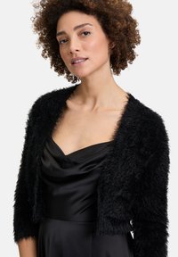 Schwarz, flauschige verkürzte Strickjacke mit langen Ärmeln, kombiniert mit einem schwarzen Satinkleid mit drapiertem Ausschnitt und glatter Textur.