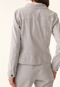 Pasiakowa bawełniana kurtka z kołnierzykiem, z guzikami i dopasowanym krojem. Tkanina ma pionowe białe i granatowe paski.