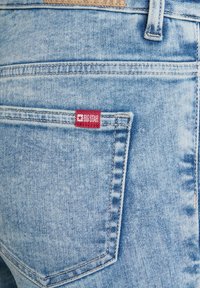 Gai zilgani denimi džinsi ar sarkano "BIG STAR" etiķeti tuvu aizmugurējai kabatai. Audumam ir viegla tekstūra ar izbalējušām vietām un šuvju detaļām.