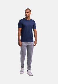 Granatowa koszulka z krótkim rękawem w kształcie V zestawiona z jasnoszarymi zwężającymi się dresami i białymi trampkami. Gładka tkanina o dopasowanym kroju.