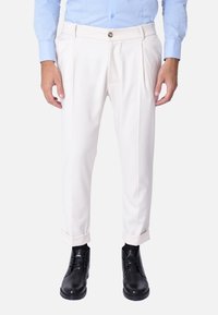 Pantaloni bianchi con pieghe, risvoltini e chiusura a bottone, abbinati a scarpe nere. Il tessuto sembra liscio e ben rifinito.
