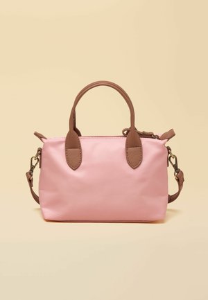 Kleine rosafarbene Handtasche mit braunen Griffen und verstellbarem Schulterriemen vor beigem Hintergrund.