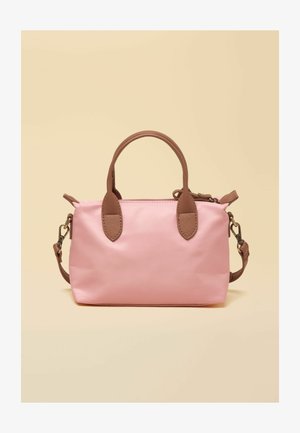 Kleine rosafarbene Handtasche mit braunen Griffen und verstellbarem Schulterriemen vor beigem Hintergrund.