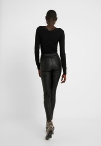 Svart långärmad topp med spetsdetaljer, parat med åtsittande svarta läderbyxor och mönstrade högklackade skor, sedd bakifrån.