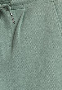 Green woven fabric featuring a textured surface, with a drawstring at the waistband and a side pocket.