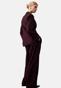 Bordeaux skræddersyet jakkesæt med en lang blazer og bredde bukser, lavet af glat stof, med slanke linjer og subtile knapper.