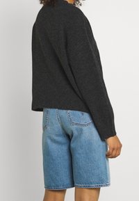 Suéter gris oscuro con un escote redondeado, combinado con pantalones cortos de mezclilla azul claro con un corte clásico y detalles cosidos en los bolsillos.