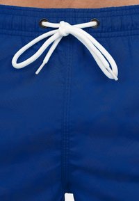 Blauwe zwembroek met een trekkoord, voorzien van witte gevlochten koord en zwarte oogjes. Glad, lichtgewicht stof, gestikte naden en geen patronen.