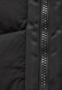Primo piano di una giacca nera isolata, con una texture in nylon liscia, sezioni gonfie e una cerniera nera centrale con denti rettangolari.