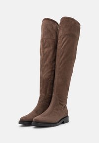 Botas de ante marrón por encima de la rodilla con una textura suave, punta redonda y cremallera lateral. Suela de goma negra y detallado minimalista.