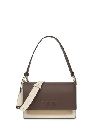 Bolso de hombro de cuero marrón y beige con correa ajustable color crema, logo "TOUS" en relieve en la solapa frontal y detalles de herrajes en tono dorado.