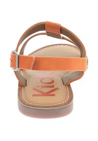 Sandal in suede arancione con suola piatta, cinturino alla caviglia regolabile e logo "Kicks" rosa su una soletta beige. Dettagli cuciti lungo i bordi.
