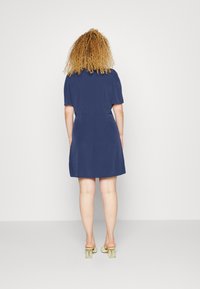 Vestido curto azul-marinho com mangas curtas, silhueta ligeiramente esvoaçante e uma textura suave, combinado com saltos verde-claro.