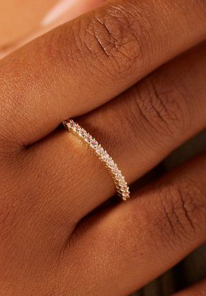 Gouden bandring met een gebogen ontwerp, bezet met kleine heldere edelstenen langs de bovenrand, die een gladde textuur tegen de huid toont.