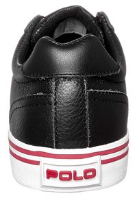 Zapatilla de cuero negra con talón acolchado, suela de goma blanca y acentos en franjas rojas. Presenta un logo blanco de "POLO" en la pestaña del talón.