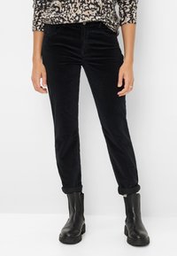 Pantalons en velours côtelé noirs au design ajusté, avec des poignets retroussés, cinq poches et une texture lisse. Associés à des bottines noires.