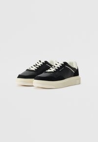 Sorte sneakers laget av semsket skinn og lær med kremfargede snørebånd og såler. Har et elegant design og sidemerking.