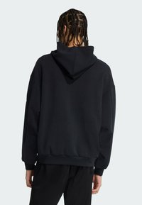 Sort oversized hoodie med snorehals, sænkede skuldre og ribbede manchetter, lavet af blødt stof, vist fra bagsiden.