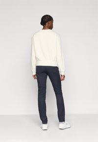 Valge särk ribatud mansettidega, kombineeritud tumedate siniste pükstega. Riietus on lihtsa kujundusega, millel on selge siluett ja peen tekstuur.