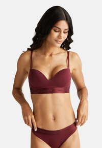 Bordeauxkleurige bh met zachte cups, dunne verstelbare bandjes en een elastische band met het merk "United Colors of Benetton".