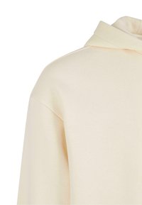 Sweat à capuche beige montrant le haut du dos et l'épaule avec des lignes de couture visibles.