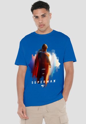 Young man wearing a blue t-shirt featuring Superman looking upward with "LOOK UP" text and cityscape background.