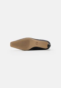 Chaussure plate en cuir noir avec une tige texturée, bout pointu et semelle en caoutchouc avec des stries pour une meilleure adhérence.