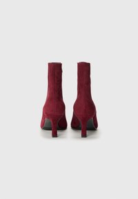 Bottines en daim bordeaux avec un talon fin, fermeture éclair, et une texture lisse. Design court et ajusté avec une semelle plate.