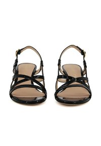 Sandali con tacco alto in vernice nera, con cinturini incrociati e fibbia regolabile alla caviglia. Soletta color beige chiaro e superficie liscia.