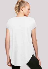 Bílý krátký rukávový top s kulatým lemem a jemnou texturou, volný střih a minimalistický design. Nosený s tmavými legínami.
