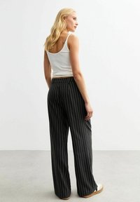 Zwarte streep brede broek met een gladde textuur, voorzien van een aansluitende tailleband en een ontspannen silhouet. Gecombineerd met een witte tanktop.