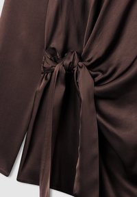 Top in satin marrone con dettaglio annodato in vita, maniche lunghe e texture liscia. Design semplice e privo di decorazioni.