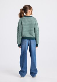 Maglione a righe verdi e blu con maniche oversize, abbinato a jeans in denim blu a vita alta e gamba larga.