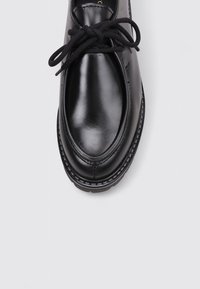 Zapato de cuero negro con un acabado suave, punta redonda y diseño tradicional de cordones. Presenta costuras visibles y una suela resistente.