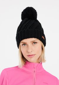 Musta neulottu pipo, jossa on teksturoitu vino kuvio ja pörröinen pompomi päällä. Mukana pieni ruskea etiketti sivussa.