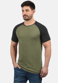 Green short-sleeve t-shirt with black raglan sleeves, round neck, textured fabric, and a fitted design. Worn with blue denim jeans.