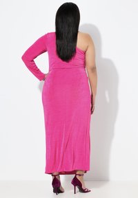 Fuksjowa sukienka na jedno ramię z długim rękawem o dopasowanym kroju, wykonana z miękkiego, teksturowanego materiału, zestawiona z fioletowymi sandałami na wysokim obcasie.