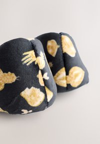 Paraorecchie in pile nero morbido con guscio giallo e motivi animali, forma arrotondata e dettagli cuciti. Tessuto strutturato che offre calore e comfort.