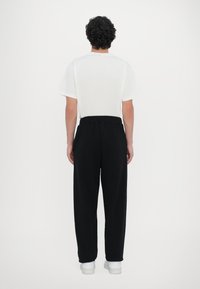 White short-sleeve t-shirt and black, loose-fitting pants with elastic waistband. The pants have a smooth texture and straight leg design.