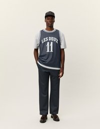 Tengerész kék és szürke csíkos póló fehér "LES DEUX" felirattal; tengerész kék csíkos nadrággal és fekete sapkával párosítva. Barna cipők teszik teljessé a megjelenést.