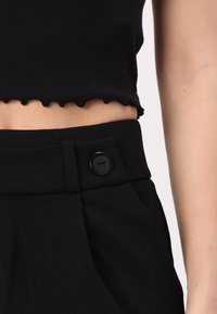 Haut court noir à côtes avec un ourlet festonné, associé à un pantalon noir taille haute avec une fermeture à bouton et des poches latérales.