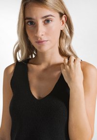 Top nero lavorato a maglia senza maniche con scollatura a V, caratterizzato da una texture a coste e spalline nere. Inquadratura ravvicinata della parte superiore del corpo del modello.
