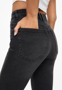 Jeans en denim noir ajustés avec une texture lisse, design à cinq poches et poches arrière proéminentes. Le tissu a un léger effet stretch pour le confort.
