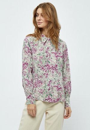 Camicia floreale a maniche lunghe con colletto a bottone. Presenta una base bianca con motivi sparsi in viola e verde. Tessuto morbido e leggero.