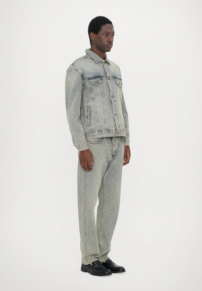 Light blue denim jacket with two chest pockets, paired with matching jeans. Both garments feature a faded design and subtle distressing. Black shoes.