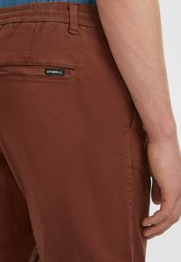 Bruine shorts met een gladde textuur, voorzien van een logopatch op de achterzak en een elastische tailleband voor comfort.