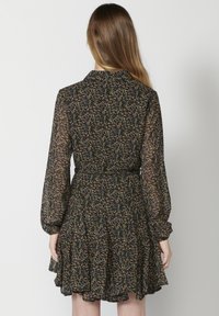Abito nero floreale con maniche lunghe, tessuto trasparente, vita arricciata e orlo a volant. Presenta un motivo floreale colorato su tutta la superficie.